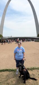 AABT President April Martin and guide dog Finn standing in front of the Saint Louis Arch, July 2026, wearing our Blind Teachers shirt from Blind Girl Designs.